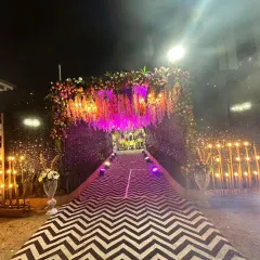We created a dramatic and glamorous entrance for a night event. This setup features a striking black and white chevron pattern walkway, flanked by sparkling walls and lit by warm candles, leading to an entryway covered in hanging flowers and purple uplighting.