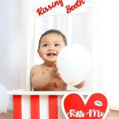 This little one is all smiles in the kissing booth, covered in lipstick marks. It's a funny and heartwarming shot that shows off his cheerful personality.