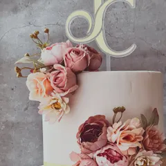 A close-up detail shot of the wedding cake, focusing on the intricate sugar flowers and the elegant custom "JC" monogram topper.