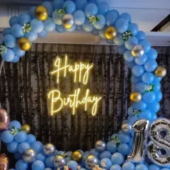 An 18th birthday setup designed with a cool blue and metallic theme. The circular balloon arch is accented with gold and silver, framing a neon sign and large "18" foil balloons to mark the special occasion.