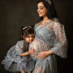Celebrating the new arrival with the whole family. This heartwarming portrait features a mother in a sparkling silver gown, with her daughter gently hugging the baby bump, showcasing a beautiful family maternity session.