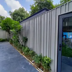 An example of a minimalist boundary wall design where material and form take center stage. The vertically grooved stone pattern is complemented by simple landscaping, creating a clean and elegant perimeter that enhances the main building's architecture.