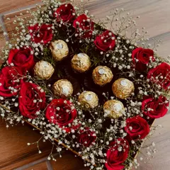 A luxurious square box arrangement featuring rich red roses, delicate baby's breath, and a centerpiece of golden Ferrero Rocher chocolates. It's a perfect blend of classic romance and sweet indulgence.