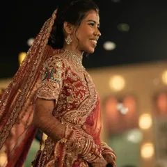 A candid shot of the bride's radiant smile during her wedding. Her intricate red lehenga and glowing makeup create a picture of pure happiness and bridal beauty.