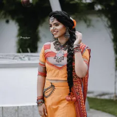 A smiling portrait of a model from a creative fashion shoot, highlighting her traditional jewelry and braided hairstyle.