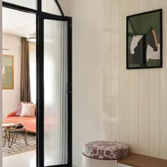As you enter the 'Colorpop Home,' you're greeted by this sleek and minimalist foyer. A fluted glass partition with an archway leads into the living room, while a duco-paneled wall conceals a seating zone and shoe storage, blending aesthetics with practicality.