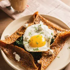 A savory crepe topped with a perfect sunny-side-up egg. The overhead angle and simple styling put the focus entirely on the delicious food.