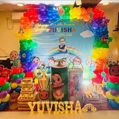 A vibrant Cocomelon first birthday party. This full-scale decoration features a rainbow balloon arch, a large themed backdrop with a personalized photo, and multiple character props.