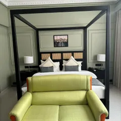 A modern hotel suite featuring a black four-poster canopy bed with a cane and wood headboard. The room is completed with a vibrant green loveseat, demonstrating my ability to work with bold colors and contemporary designs.