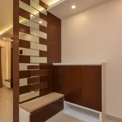 A functional foyer design with a built-in shoe rack that includes a comfortable seating bench. The partition wall with wood and mirror panels adds a decorative touch while separating the entryway from the main living area.