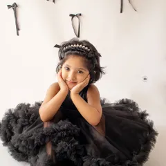 A stylish and classic portrait of a little girl in a stunning black ruffled dress. The simple white background with black bows adds a modern, graphic touch.