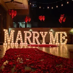 A classic terrace proposal decoration featuring our large marquee 'MARRY ME' letters. We created a dramatic entrance with a long path of red rose petals, leading up to the main display.