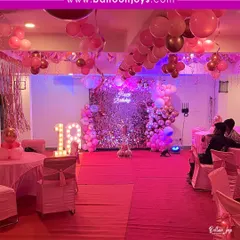 Stepping into adulthood with a splash of pink! This 18th birthday party is all about glamour, with a silver sequin wall, pink balloon arch, and large light-up marquee numbers.