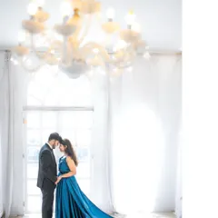 An artistic silhouette of a couple in a beautiful, high-ceilinged room with a chandelier, the bride's long blue train creating a sweeping visual effect. This shot emphasizes elegance and drama.