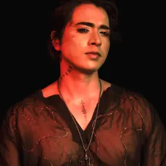 A dramatic shot of the male model under red lighting, showcasing the edgy, editorial style of the makeup.