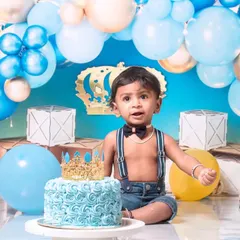 A little prince celebrating his first birthday with a royal blue cake smash. The setup includes a crown, balloons, and a delicious-looking cake ready to be smashed.