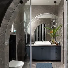 A bold and dramatic bathroom featuring dark grey marble walls in a herringbone pattern. The arched glass shower enclosure and curved vanity soften the strong materials, creating a space that is both moody and elegant.