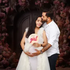 A happy couple in the studio announcing "It's a GIRL" with a cute sign. The romantic floral backdrop and their joyful interaction make this a perfect announcement picture.