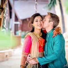A sweet and colorful portrait of a couple sharing an affectionate kiss on the cheek. The vibrant traditional outfits and the natural setting create a beautiful, happy scene.