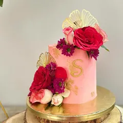 This cake is a whole vibe! A tall, modern birthday cake in a vibrant pink, decorated with fresh red and purple flowers, gold accents, and a custom monogram. The flavour is a refreshing mix of exotic fruits.
