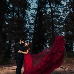 A dramatic and romantic shot of a couple in a wooded area by the beach. The deep red flying gown's train is tossed in the air, creating a beautiful, dynamic frame around them.