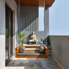 For this balcony, we created a serene meditation corner featuring a simple wooden swing. The space is anchored by a Buddha statue set against a textured grey wall, creating a peaceful and minimalist retreat.