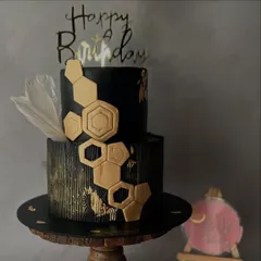 For a bold and modern statement, this two-tier black fondant cake features a striking gold honeycomb design and a wood-grain texture on the bottom tier. A single white feather adds a touch of softness to this contemporary piece.