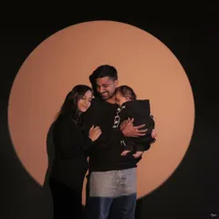 A modern family portrait using dramatic spotlighting. The family huddles together in a circle of light, creating a feeling of warmth, closeness, and being in their own special world.