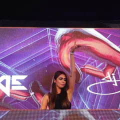 A stunning shot of me at a Delhi wedding, with one hand raised as the beat drops. The vibrant purple visuals on the LED screen behind me add to the festive atmosphere.