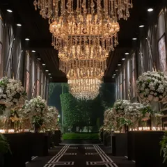 For a glamorous 25th-anniversary celebration, I designed this dramatic entryway. A grand hallway lined with massive crystal chandeliers and lush white floral arrangements set a sophisticated, high-energy tone for a night of black-tie opulence and dancing.