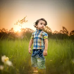 A striking portrait of a boy standing in a field of tall grass during golden hour. The beautiful backlighting highlights his hair and creates a magical, dreamy atmosphere.