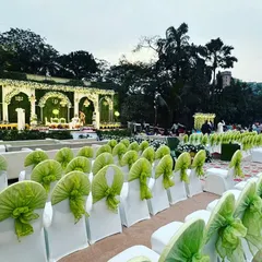 A wide view of an elegant outdoor wedding reception at The Acres Club lawns. The grand stage is complemented by neat rows of seating with lime green accents, ensuring every guest has a great view.