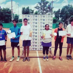 A group photo of all the winners and runners-up from the AITA TS7 Under-14 tournament, celebrating their achievements with trophies, medals, and certificates.