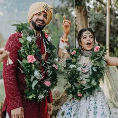 The pure joy of the jaimala ceremony. This candid shot captures the couple's happiness and excitement, surrounded by lush greenery garlands, right after becoming husband and wife.