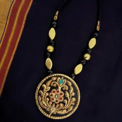 This elegant black and gold pendant showcases intricate floral gesso work, highlighted with real Tanjore gold foil and a single gemstone. It is paired with brushed gold and black beads for a sophisticated look.