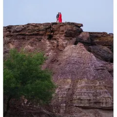 A dramatic, wide-angle shot showing the couple standing atop a rocky cliff in Jaisalmer. The scale of the landscape emphasizes the epic nature of their love story.