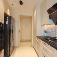 A galley-style classic kitchen with off-white profiled cabinets and a contrasting black countertop. The design cleverly integrates a tall unit beside the refrigerator for maximum storage.