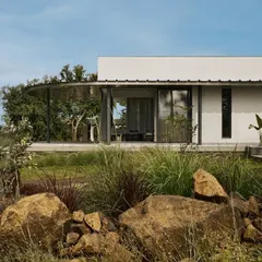 The exterior of Pavilion House showcases a blend of materials, including white brick, dark stone, and expansive glass, all nestled within a resilient desert garden. The low-lying form respects the landscape, ensuring the home feels like a natural part of its environment.