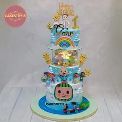 This grand three-tier Cocomelon cake includes a toy train circling the base. The 5kg chocolate cake is packed with details like a fondant boy topper, a light-up spacer, and colorful characters.