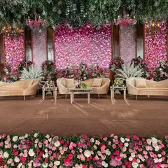 The main stage for the regal wedding, featuring a stunning backdrop made entirely of fresh pink and white roses. The plush, neutral-toned furniture was chosen to complement the vibrant floral wall, creating a perfect setting for photographs.
