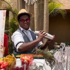 One of our bartenders in action, shaking up a fresh, fruity cocktail at a sundowner event. The bar is stocked with a colorful array of fresh-cut fruits like strawberries and dragon fruit.