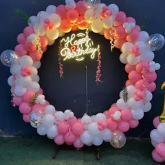 A classic circular balloon arch in pink and white, perfect for any birthday celebration. The "Happy Birthday" neon sign in the center adds a modern touch.