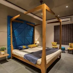 A modern take on a classic four-poster bed. The bold blue geometric headboard adds a pop of color and texture against the concrete-finish wall, creating a look that is both edgy and comfortable.