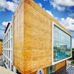 The recently completed Commercial Faculty building on Kanakpura Road. The facade features a bold juxtaposition of a large, wood-textured volume against a framed glass window, creating a modern landmark for the educational institution.