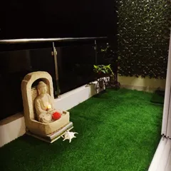 Less is more in this minimalist zen balcony. A simple stone Buddha water fountain provides a soothing sound, complemented by a lush artificial grass floor and a small vertical garden for a touch of green.