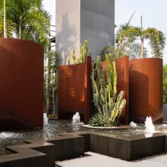 A sculptural water feature at the KEUS commercial hub. The design contrasts the industrial feel of rust-hued Corten steel walls with the organic forms of cacti and the movement of water, creating a bold, avant-garde landscape.