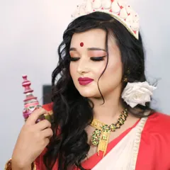 A portrait of a traditional Bengali bride, highlighting the intricate details of her makeup, the 'mukut' headwear, and the red and white saree.