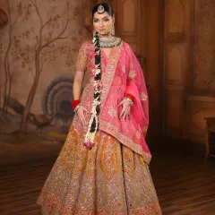 A breathtaking full-length shot of a bride in a vibrant pink and orange lehenga. The makeup is kept fresh and radiant to match the colorful outfit, complete with a long floral braid.