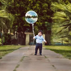 A simple and beautiful outdoor portrait to mark a first birthday. This little boy holds a single, large balloon on a path surrounded by greenery, creating a timeless and classic image of childhood.