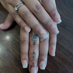 We specialize in delicate, hand-painted nail art for a touch of understated beauty. This close-up shows intricate white floral details on a sheer, natural-looking nail extension, perfect for an everyday elegant style.